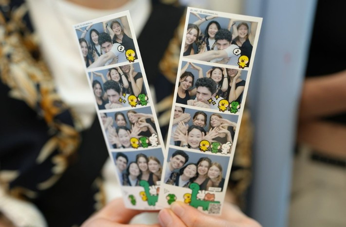 Các bạn trẻ đang vui vẻ tạo dáng chụp ảnh trong một không gian photo booth được trang trí bắt mắt với tông màu hồng và đèn neon