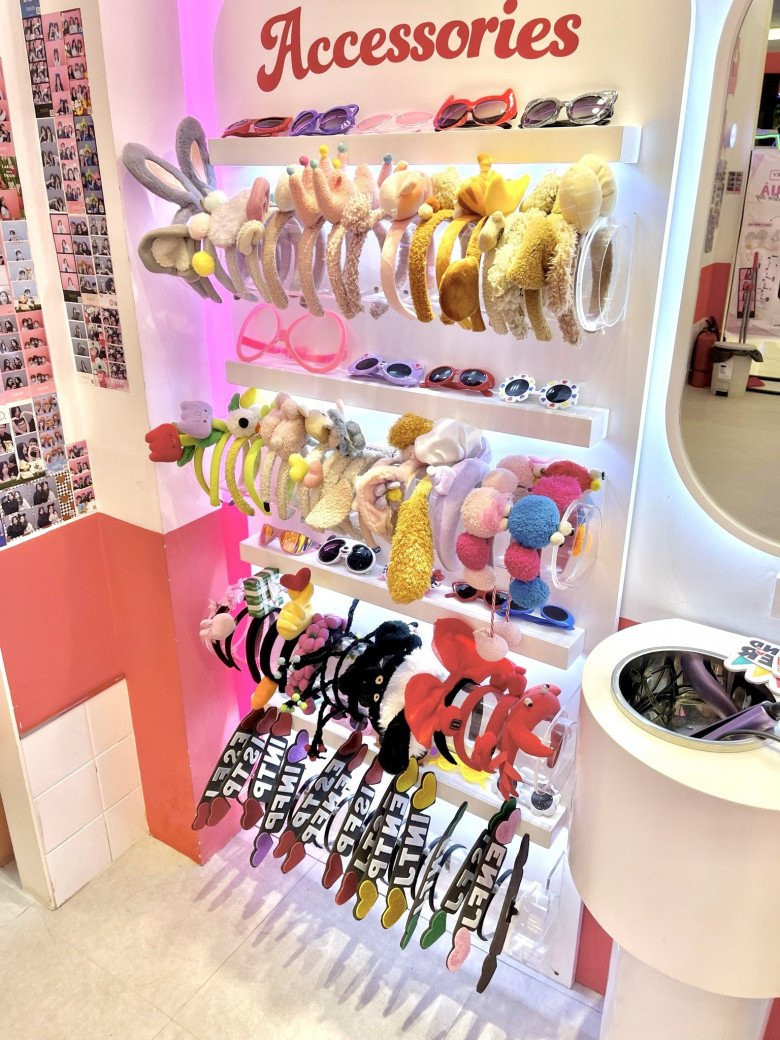 Hai bạn nữ trẻ chụp ảnh thân thiết trong buồng photo booth, với ánh sáng vàng ấm áp và phụ kiện mũ dễ thương