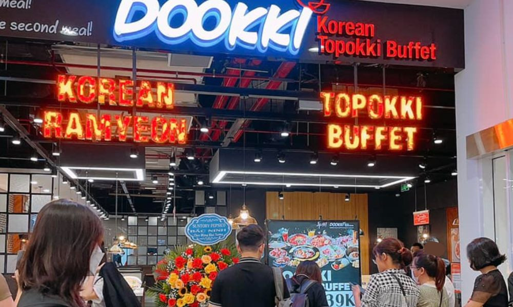 Thực khách đang tự tay lựa chọn các loại topping và nước sốt tại quầy buffet Dookki, thể hiện sự tự do trong việc sáng tạo món ăn.